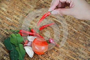 Hand holding one red chili pepper over old basketwork background