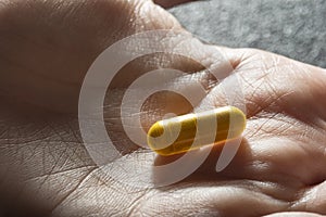 Hand holding one yellow medicinal tablet