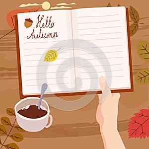 Hand holding an open Autumn Daily Diary notepad, list schedule, goals, to do, acorn, autumn leaves, coffe cup. Personal