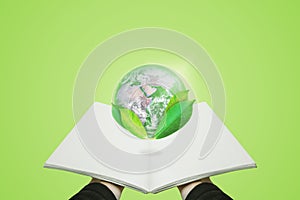 Hand holding opened book with globe with leaves, on green background. Element of this image are furnished by NASA