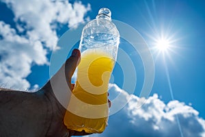 Hand holding Orange lemonade towards sun and blue sky