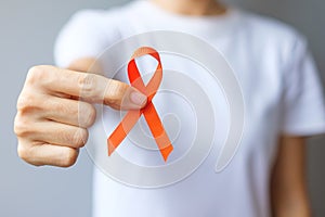 Hand holding Orange Ribbon for Leukemia, Kidney cancer day, world Multiple Sclerosis, CRPS, Self Injury Awareness month.