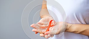 Hand holding Orange Ribbon for Leukemia, Kidney cancer day, world Multiple Sclerosis, CRPS, Self Injury Awareness month.