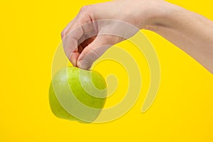 Hand holding organic green delicious apple Isolated on yellow Background. Healthy eating and dieting concept