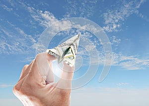 Hand holding an origami dollar paper airplane with blue sunny sky -- financial goal investing concept