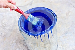 Hand Holding Paint Brush Over Paint Bucket