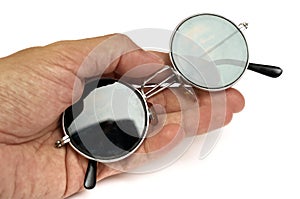 A hand holding a pair of round glasses with skull impression embedded white backdrop