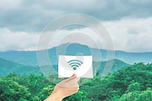 Hand holding paper with cutout wireless signal in green natural background.