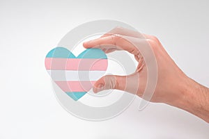 Hand holding a paper heart with transgender flag on white background