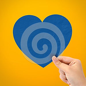 Hand holding paper heart on yellow background