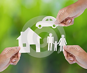 Hand holding paper home, car, family on green background