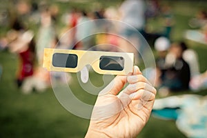 Hand holding paper solar eclipse with blurry crowd people watching totality show picnic yard, Dallas, Texas, April 8