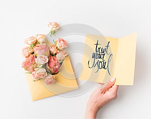 hand holding paper with TRUST YOUR SOUL sign beside pink flowers in envelope