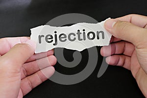 Hand holding a paper with written word rejection in black background. How to handle rejection concept.