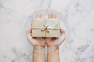 Hand holding parcel gift box, on white marble stone table background