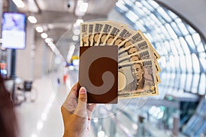 Hand holding a passport with ten thousand Japanese yen bills at the airport