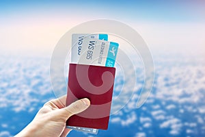 Hand holding a passport and two air tickets on a blue background of cloudy sky. Travel and vacation in beautiful places