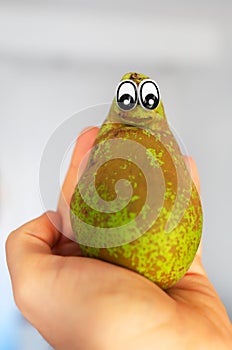 Hand holding a pear with eyes.