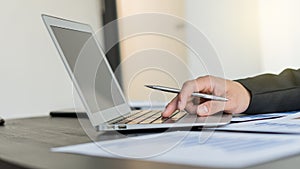 The hand holding a pen of a businessman working on a laptop with a graph is placed on the table with a blurred