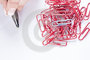 hand holding a pen and a collection of paperclips on a white surface