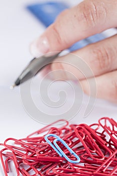 hand holding a pen and a collection of paperclips on a white surface