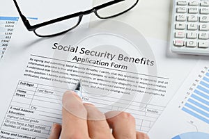 Hand holding pen over social security benefits form