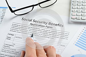 Hand holding pen over social security benefits form photo