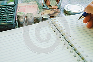 Hand holding a pen to write on the blank notebook with banknotes