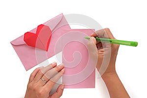 Hand holding a pen and writing a letter with red heart paper origami and pink envelope