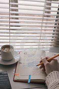 Hand holding pen writing notebook. There are a cup of coffee