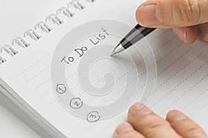 Hand holding pen writing what to do in personal to do list note pad on white table using as task list, things to complete and