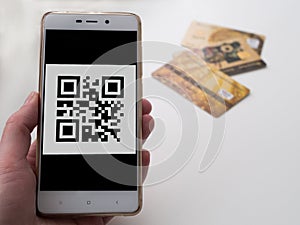 Hand holding phone with barcode on the screen. Credit cards on background