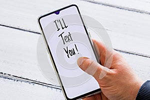 hand holding a phone with the words `I`ll text You!` Light wooden background