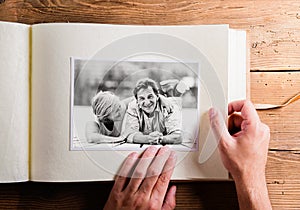 Hand holding photo album with pictures of senior couple. Studio
