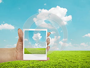 Hand holding photograph of landscape with landscape in background