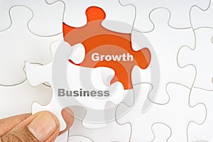 Hand holding piece of jigsaw puzzle with word BUSINESS GROWTH.