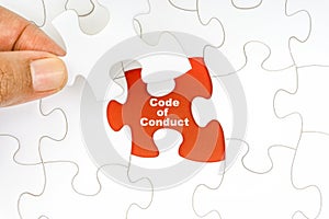 Hand holding piece of jigsaw puzzle with word CODE OF CONDUCT