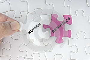 Hand holding piece of jigsaw puzzle with word HUMAN RESOURCE.