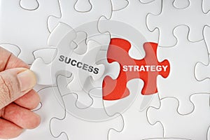 Hand holding piece of jigsaw puzzle with word SUCCESS STRATEGY