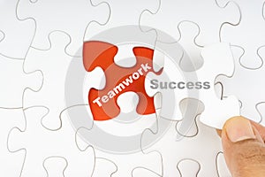 Hand holding piece of jigsaw puzzle with word SUCCESS TEAMWORK