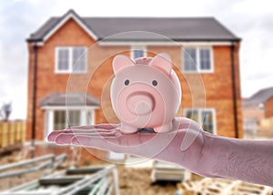 hand holding piggy bank against blurred semi-detach house