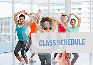 Hand holding placard with class schedule text against women dancing in background