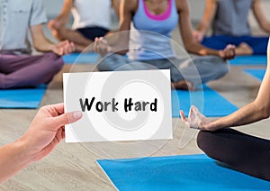 Hand holding placard that reads work hard against people doing meditation