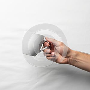 A hand is holding a plain white ceramic mug against a white background