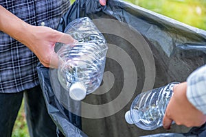 Hand holding plastic bottles waste, Couple picking up trash putting to the black garbage bag at Sunflower Park on Environmental