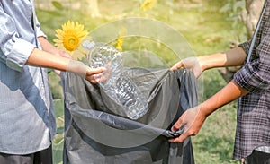 Hand holding plastic bottles waste, Couple picking up trash putting to the black garbage bag at Sunflower Park on Environmental