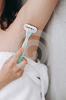 Hand holding plastic razor and shaving hairy armpit. Young woman shaving armpits with plastic razor closeup in home bathroom. Skin