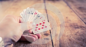 A hand holding playing cards on o vintage wooden table | Gambling | Gambler