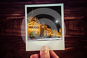 Hand holding polaroid postcard of Flinders Street Station at night. Melbourne, Australia. Travel memories scrapbooking of good ti