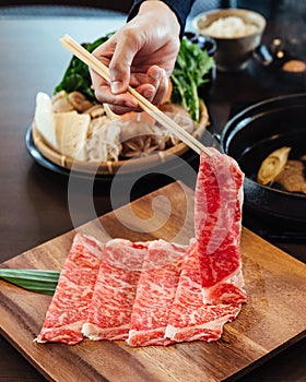 A hand holding Premium Rare Slices Wagyu A5 beef with high-marbled texture with chopsticks on square wooden plate.